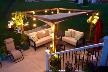 Reviewer's backyard at night, with the canopy above a wooden frame that is covered in twinkle lights 