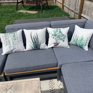 Reviewer's gray sectional on the patio with four greenery pillows