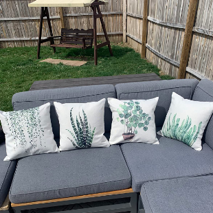 Reviewer's gray sectional on the patio with four greenery pillows