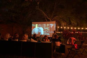 Review image of an outdoor movie party with the screen in use and half a dozen people watching it 
