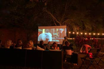 Review image of an outdoor movie party with the screen in use and half a dozen people watching it 