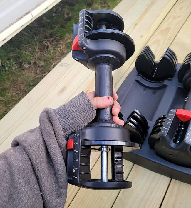 reviewer holds a black adjustable dumbbell in their hand