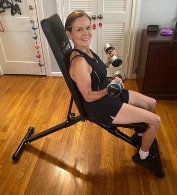 reviewer sits on black adjustable weight bench while doing bicep curls