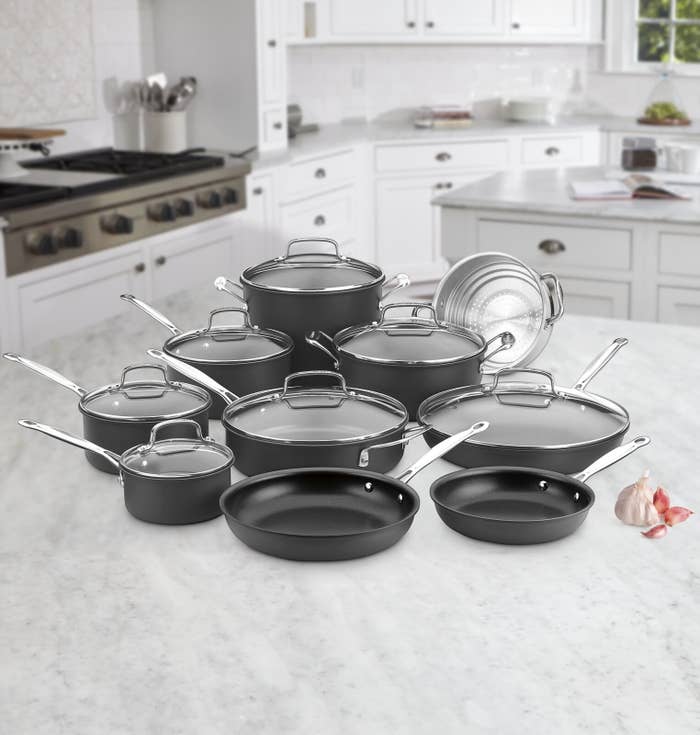 The pans, pots, and skillets, which are all a dark gray color, with metal handles and clear glass lids