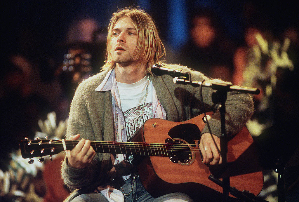 Kurt sitting with a guitar at a microphone