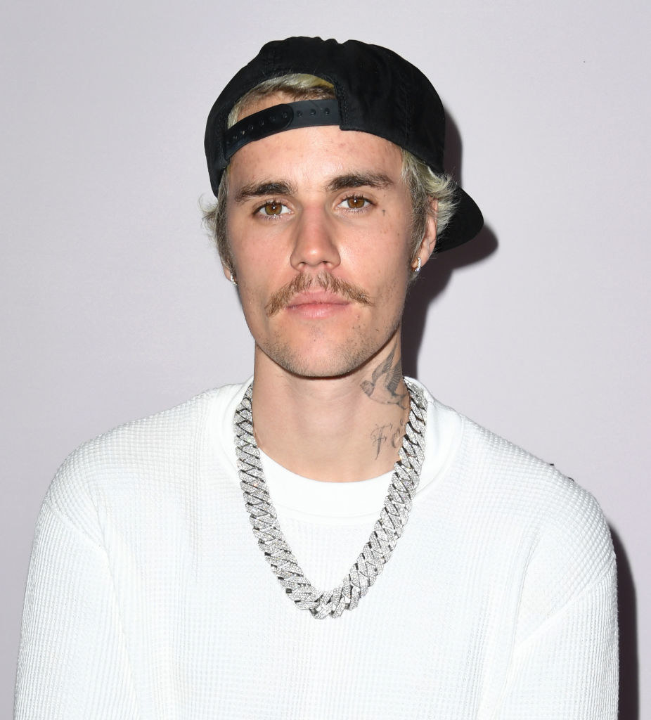 Justin wearing a backward cap, thick silver chain, and white sweater