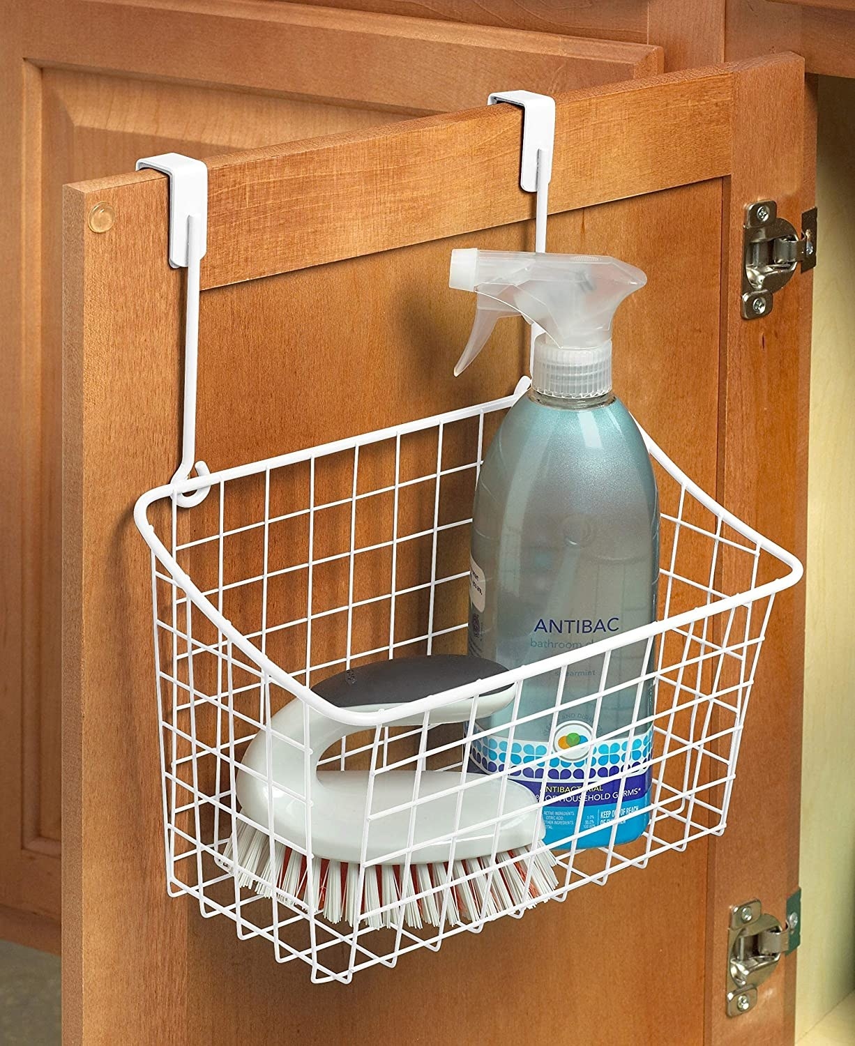 a basket hanging off of a cabinet with cleaning supplies in it 