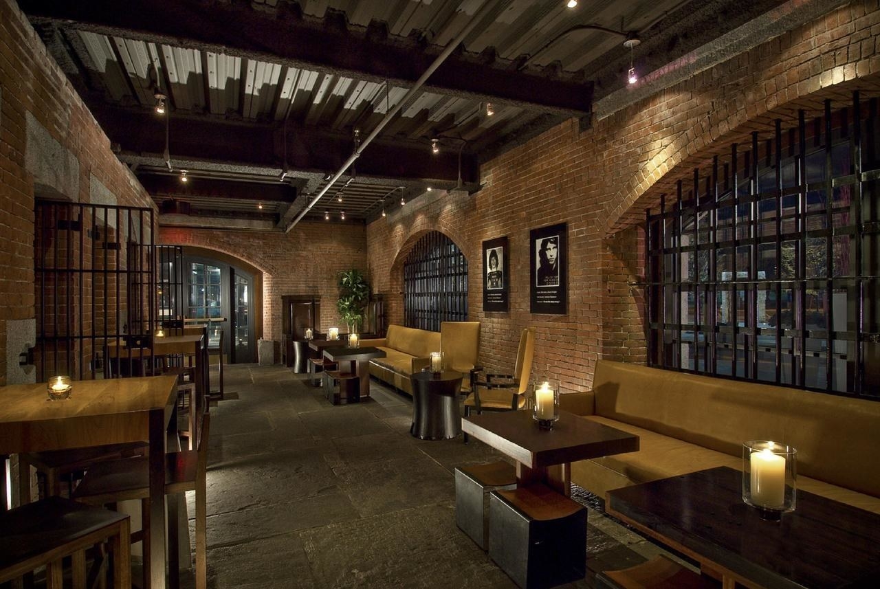A hotel bar with low lighting, brick walls, steel bars, and an open jail cell 