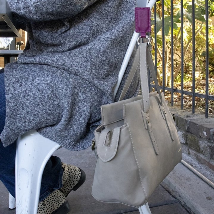 the leather bag hanging from the violet bagnet which is stuck to a metal chair