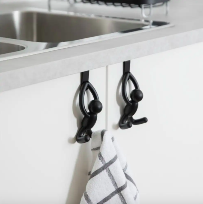 A pair of stick-figure shaped hooks hung over a kitchen cabinet