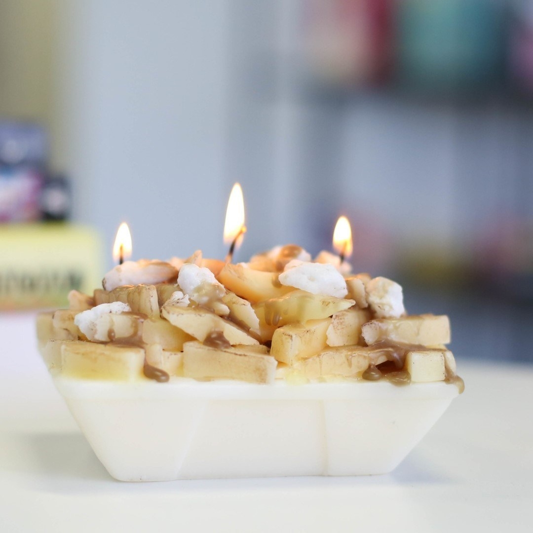 A small candle in the shape of a box filled with poutine