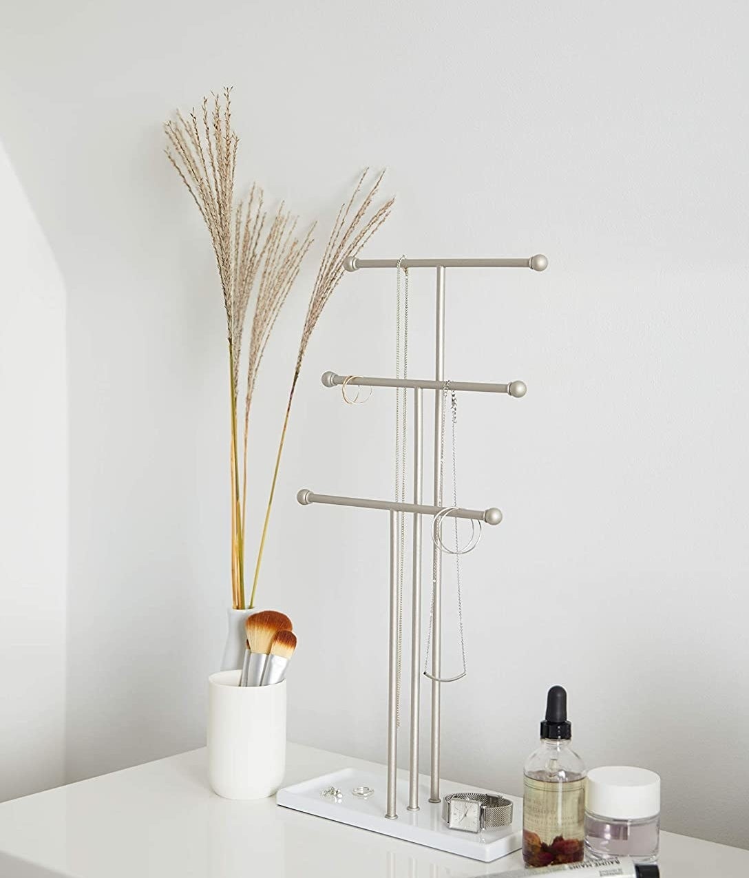The jewelry stand on a minimalist vanity with necklaces hanging off of it 