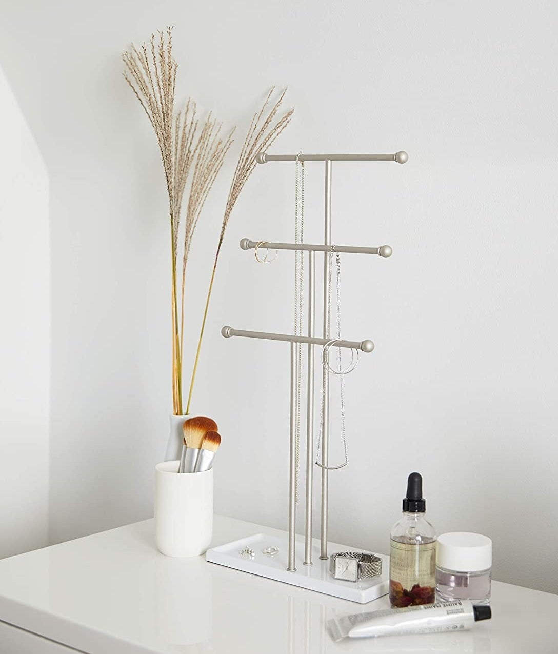 The jewelry stand on a minimalist vanity with necklaces hanging off of it