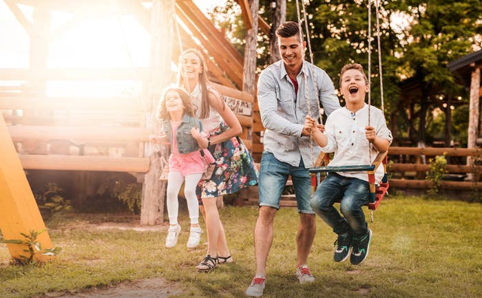 Mother and father pushing young son and daughter on swings at sunset