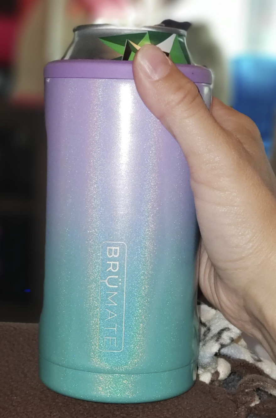 reviewer holding a can in the insulator which is an ombre color that moves from lavender to seafoam green wth iridescent glitter 