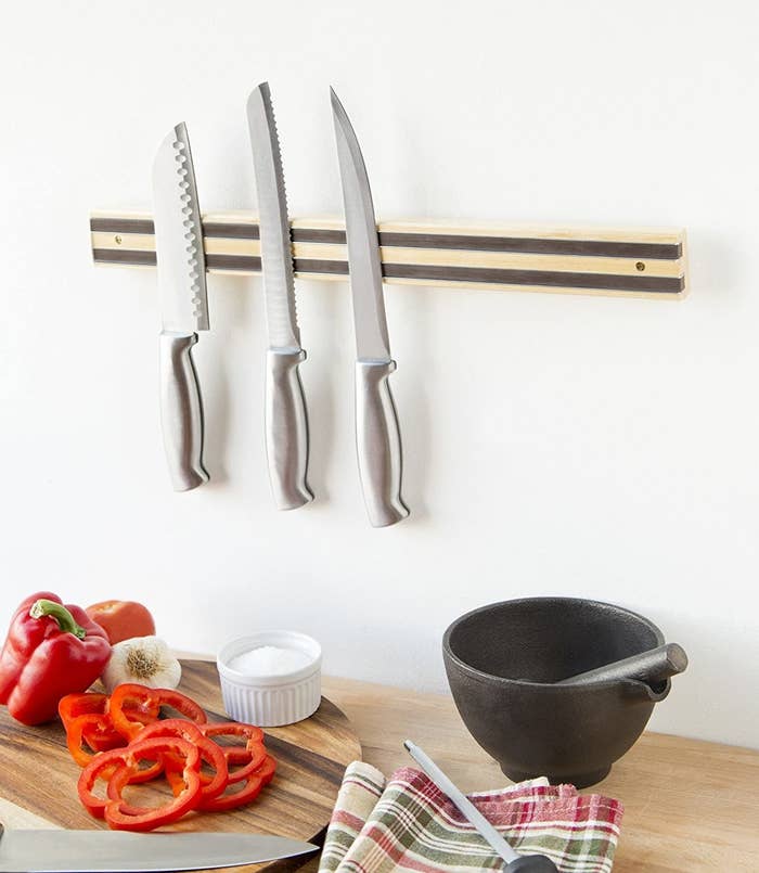 The knife bar on a wall in a kitchen holding up three large knives