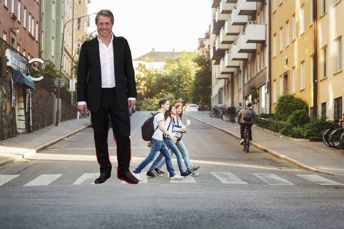 Hugh Grant made to look like a giant standing next to average-size people who are crossing a street