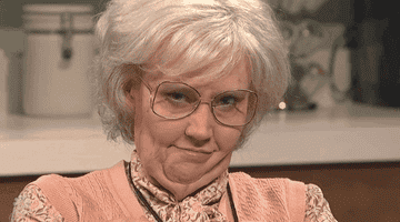 Kate McKinnon dressed as an old woman and winking