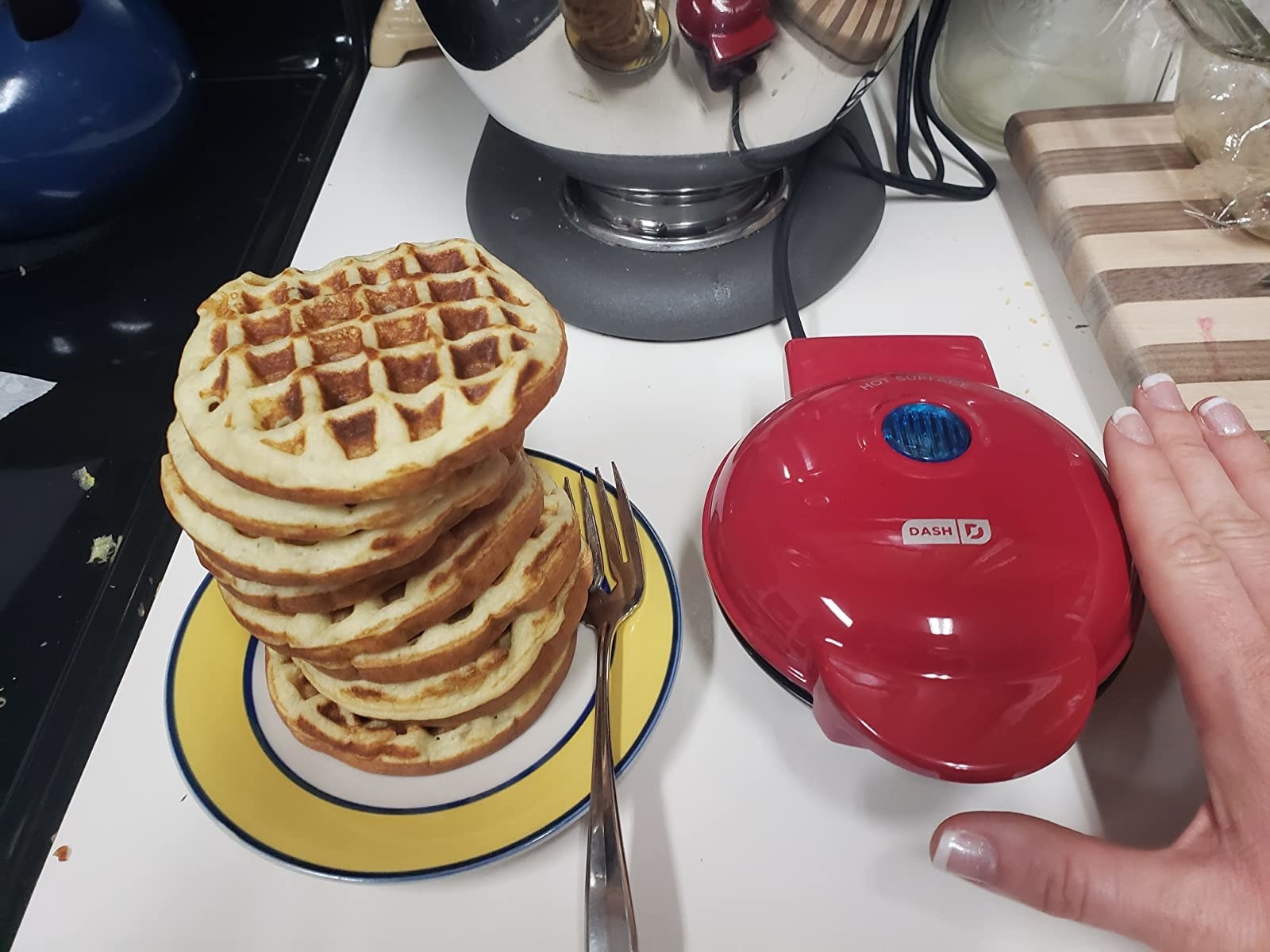 a reviewer&#x27;s small red waffle maker next to a pile of waffles