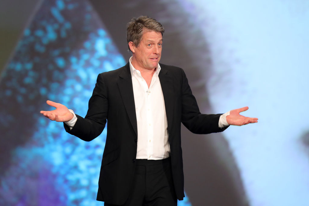 Hugh in a shirt and jacket, no tie, holding his hands out in a &quot;What?&quot; gesture