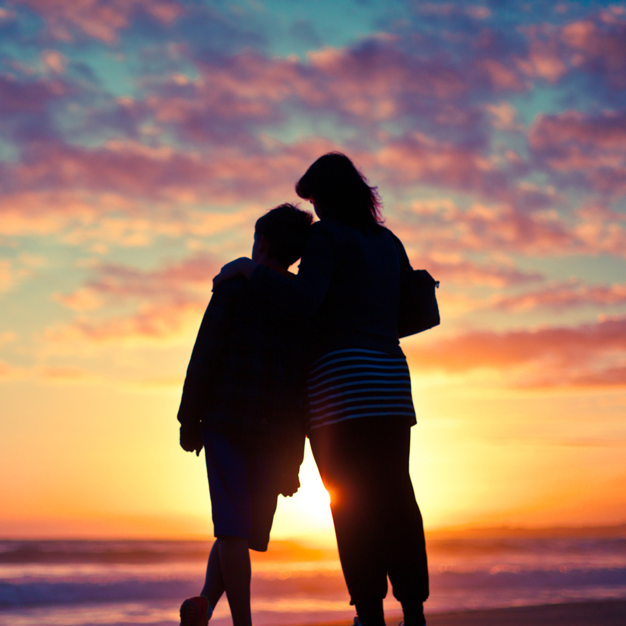 Mother and son standing at ocean&#x27;s edge at sunset