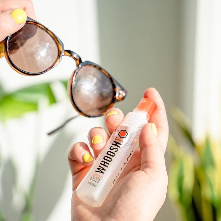Someone spritzing the cleaner onto a pair of smudgy sunglasses