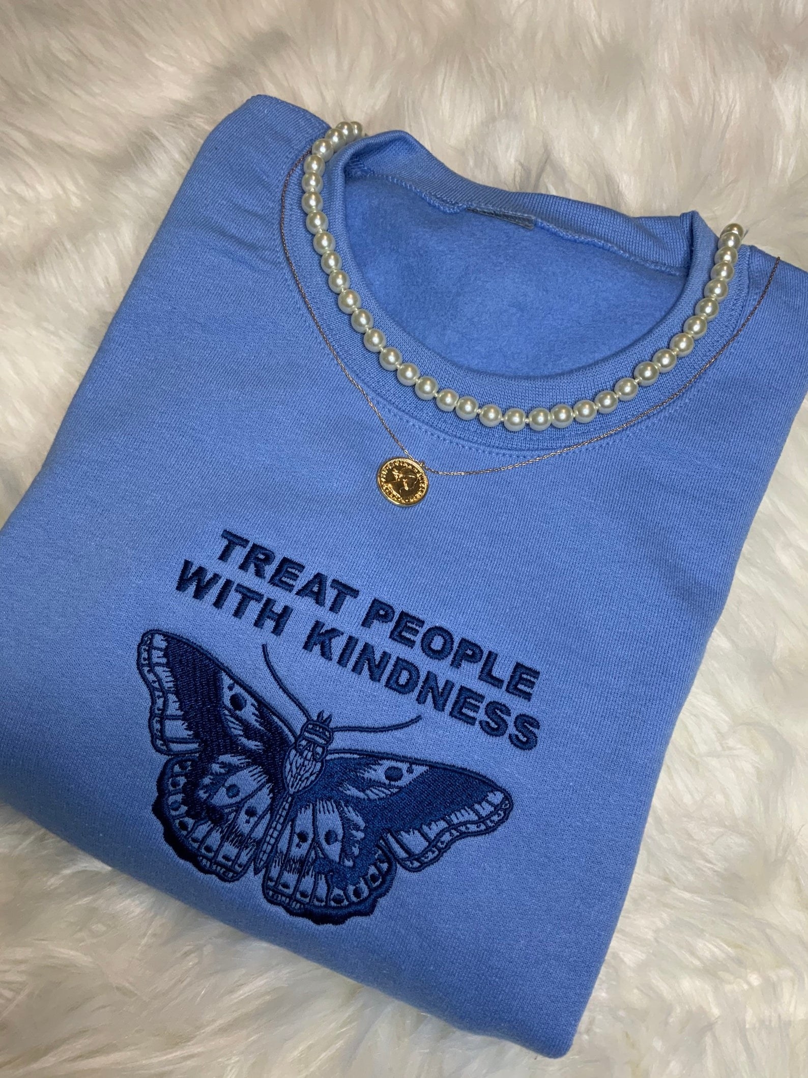 blue crewneck sweater with a butterfly and the quote &quot;treat people with kindness&quot; embroidered on it