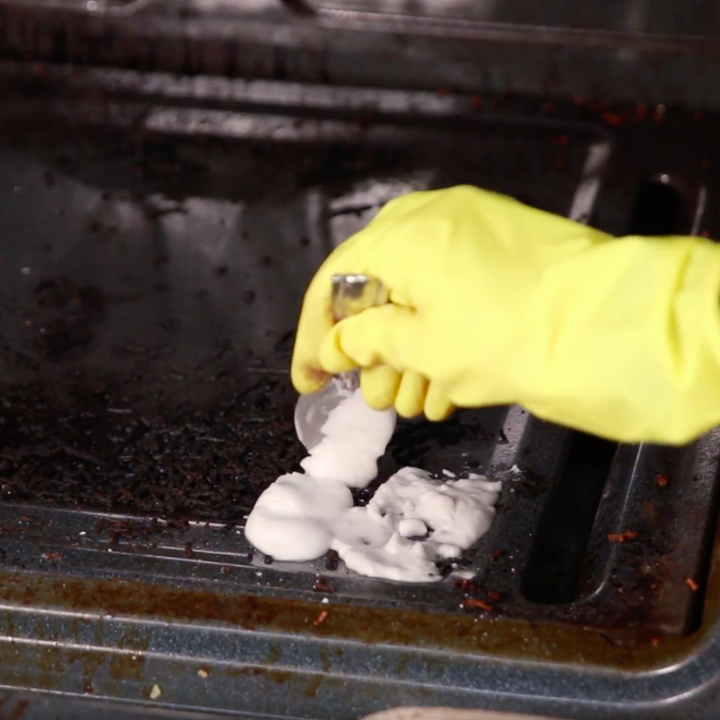 yellow-gloved hand spoons paste onto oven door 