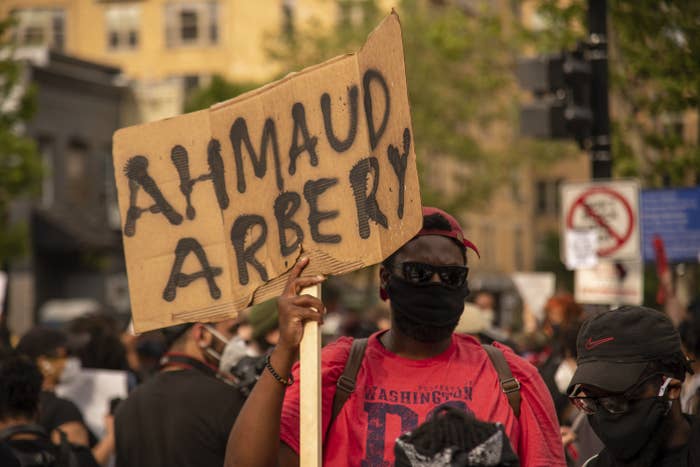 A man at a demonstration holds up a cardboard sign with Ahmaud Arbery's name