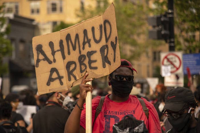 A man at a demonstration holds up a cardboard sign with Ahmaud Arbery&#x27;s name