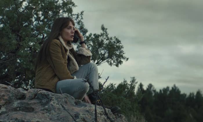 Angelina talks on the phone while sitting on a rock in the forest