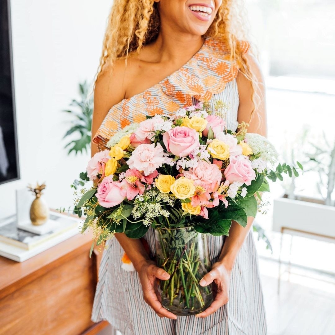 A person holding a large glass vase full of flowers