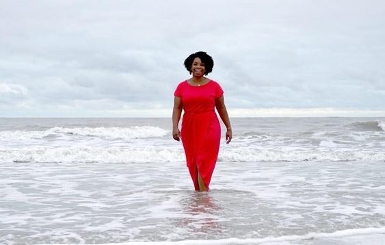 a reviewer wearing the dress in red on a beach