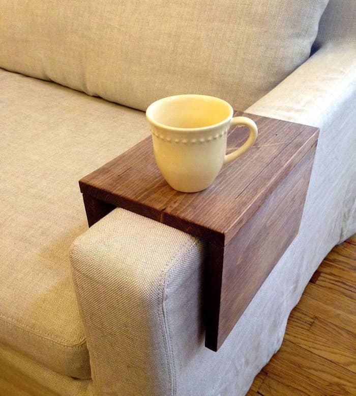 Wooden arm rest table installed on couch with coffee cup on top