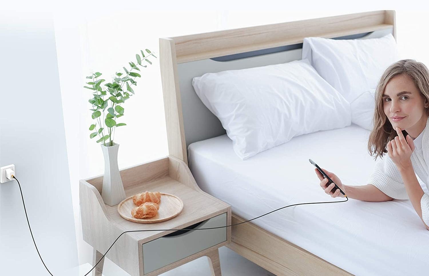 person lying on the bed with their phone lugged in via long charger
