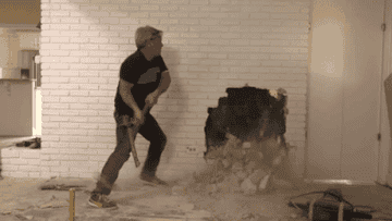 Guy demolishing brick wall with sledgehammer