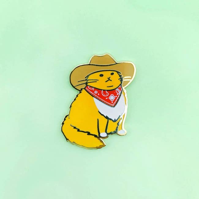 a pin of a gold cat wearing a cowboy hat and bandana