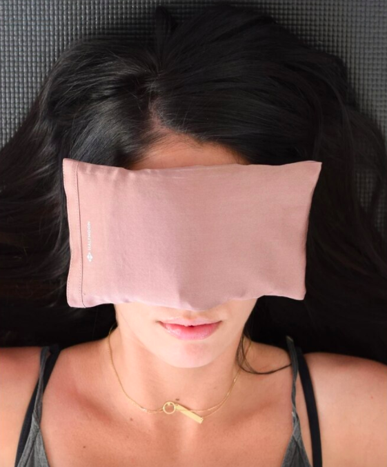 A person lying on a bed with the eye pillow over their face