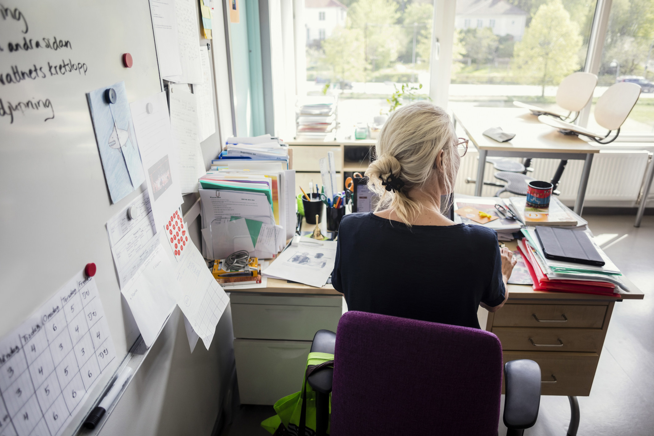 A rear view of a teacher working at their desk in a classroom