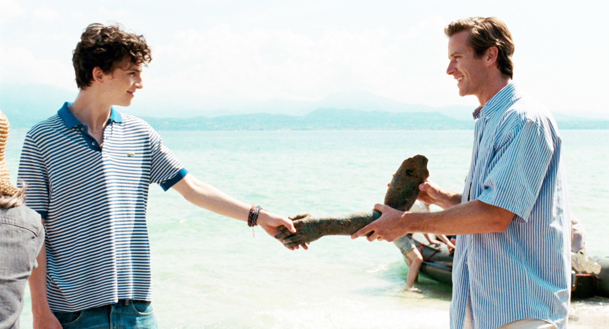 Timothée Chalamet and Armie Hammer look at each other as they hold a piece of driftwood