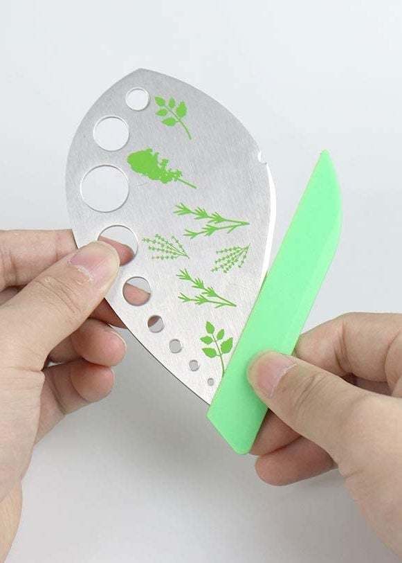 A person holding the herb stripping blade, removing the silicone guard to reveal its sharp bladed edge 