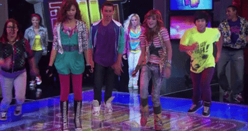 The Shake It Up cast dances on stage in glittery, patterned, neon clothes