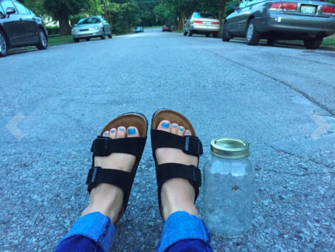a reviewer wearing the sandals in black and sitting in the street