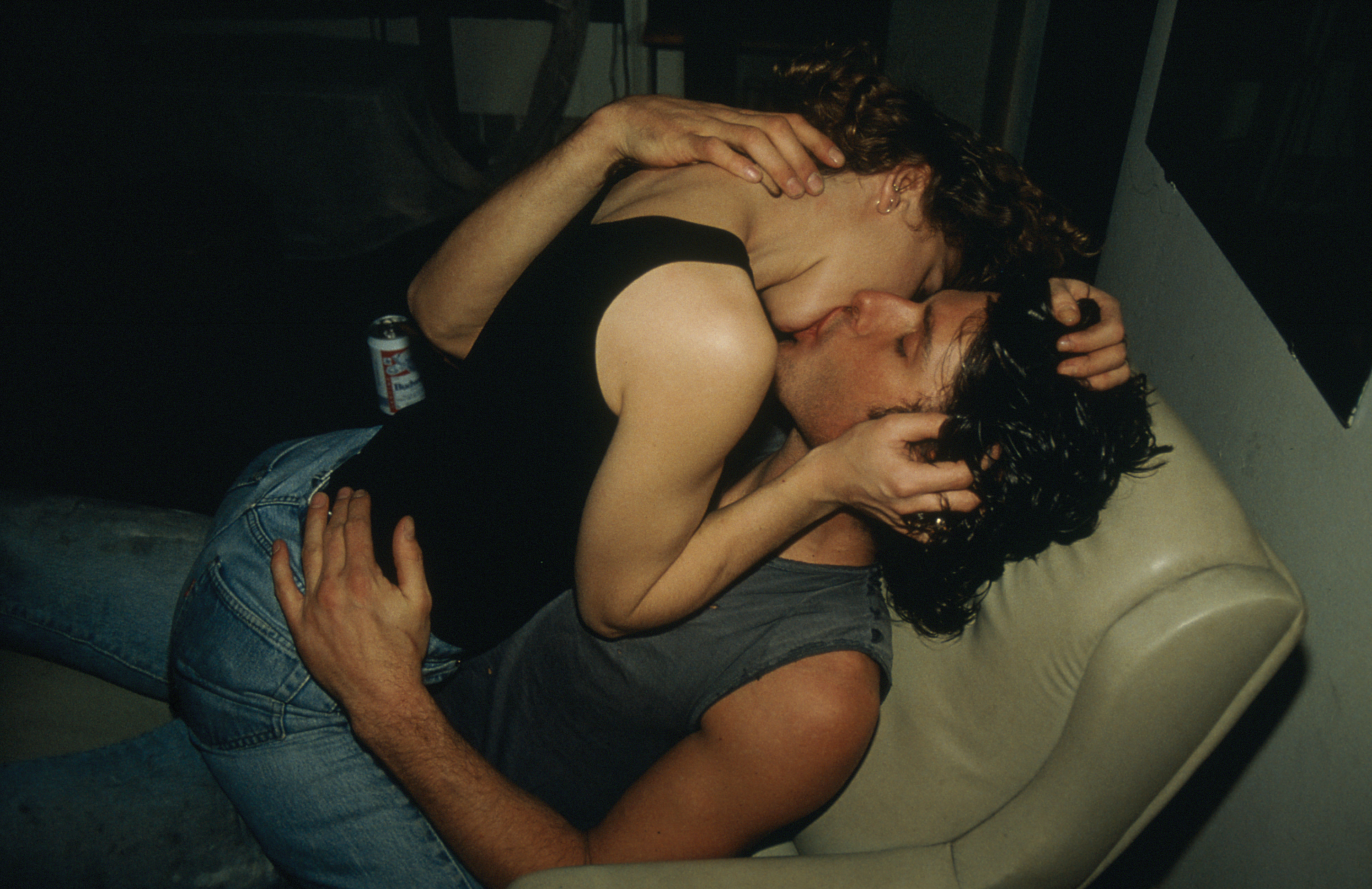 Two young people in jeans passionately kissing on a white leather chair