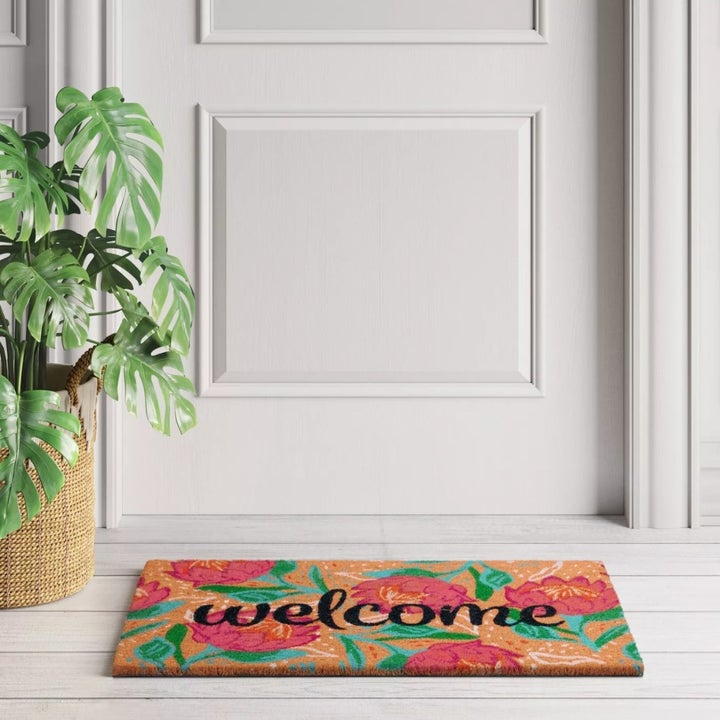 The 'welcome' doormat in black lettering with a floral background on a doorstep