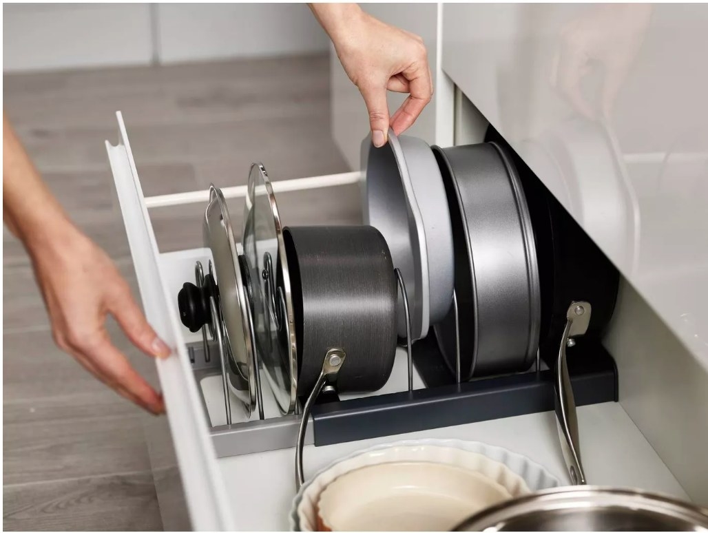 A grey expandable cookware rack filled with pots, pants, and cake tins