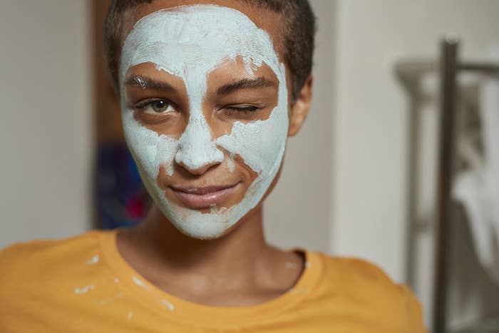 Close-up portrait of young woman with facial mask winking at home