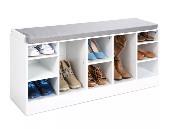 A white bench with a grey foam cushion atop and 10 compartments below to store shoes and boots