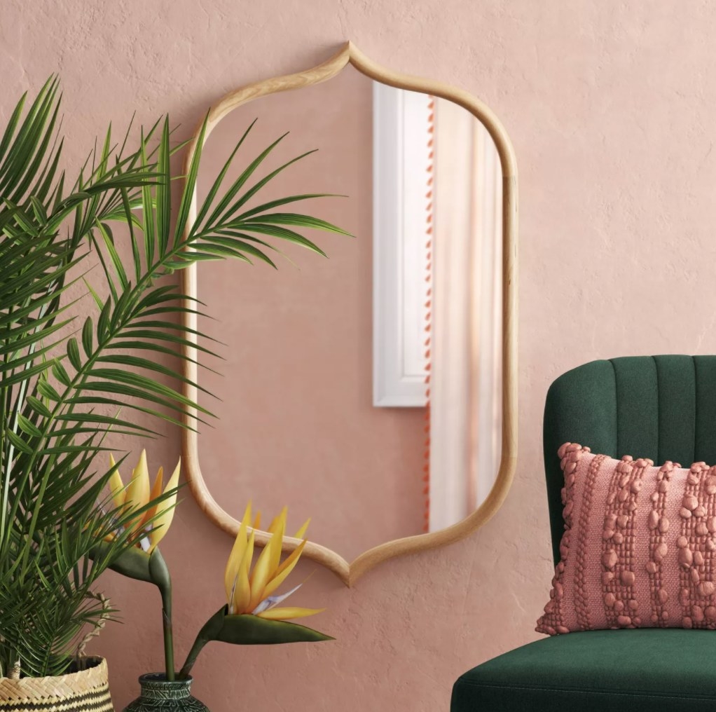 The mirror against a salmon colored wall framed by a large plant and green chair