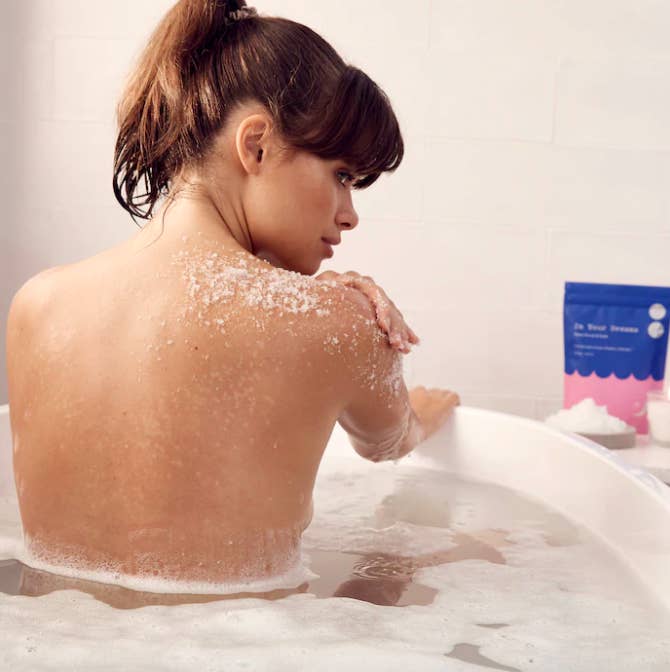 A person using the scrub in a foamy bath